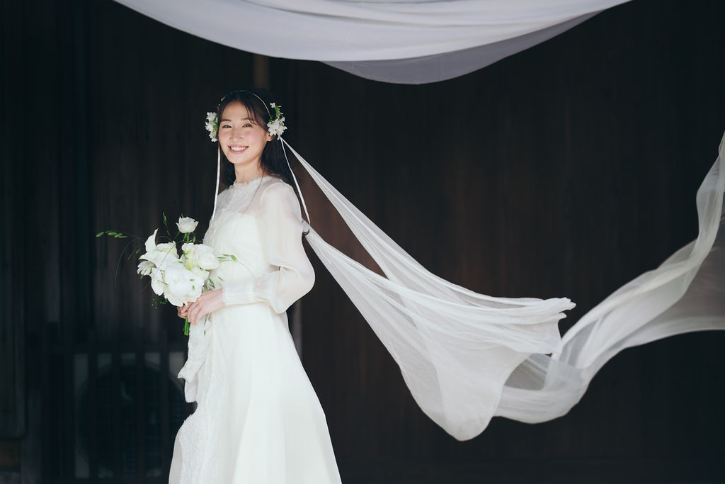 古民家の高砂席に並ぶ新郎新婦と、庭の緑を望む和の披露宴空間