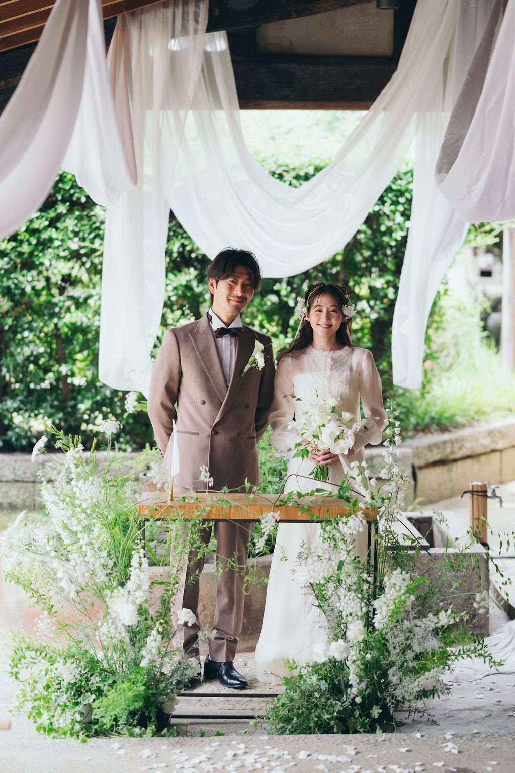 白い布が舞う人前式の祭壇に立つ新郎新婦と季節の花