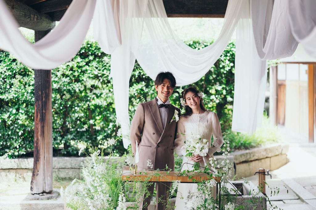 白い布が舞う祭壇に並ぶ新郎新婦、白い花に囲まれた人前式の引き